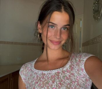 Atractiva modelo australiana Steph Mandich posando con un vestido floral de encaje blanco y dorado, con una sonrisa cautivadora y actitud sensual