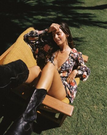 Modelo australiana Steph Mandich posando con un vestido floral y botas negras de cuero sobre un fondo de césped verde