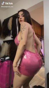 Videos Karely Ruiz en pose lateral que resalta sus curvas y piernas torneadas con un vestido rosa ajustado