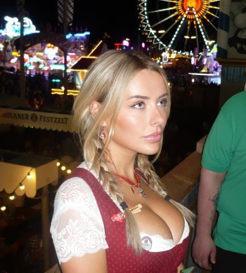 Corinna Kopf, una hermosa influencer rubia con un vestido tradicional bávaro rojo y blanco, posando en un parque de atracciones nocturno