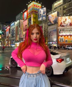 Modelo pelirroja Helen Grube con atuendo llamativo, pose atrevida y fondo urbano de Japón