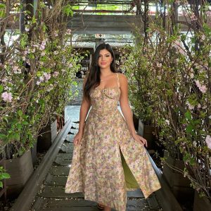 Modelo Rosana Hernandez posando elegantemente en un entorno natural con flores y vegetación, luciendo un vestido floral con diseño vintage y detalles brillantes