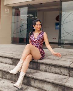 Kelly Bustamante posa en escaleras con un vestido morado brillante y botas altas blancas