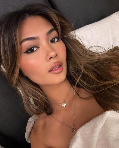 Audrey Thompson, una joven influencer con cabello castaño ondulado, maquillaje natural y un abrigo blanco de lana