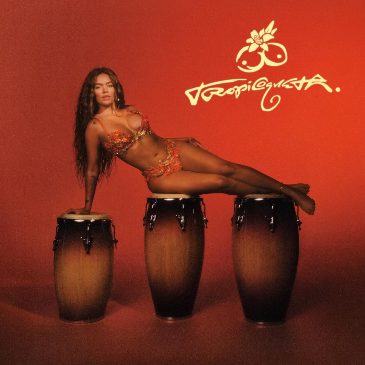 Karol G recostada sobre tres tambores en una imagen promocional del disco Tropicoqueta