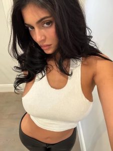 Kylie Jenner con cabello oscuro y rizado, posando de manera sugerente en atuendo blanco