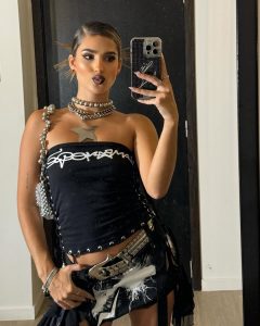 Julieta Poggio posando con un teléfono celular en la mano, luciendo un atuendo negro con accesorios llamativos