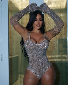 Karishna Ayala con brazos alzados, luce un bodysuit brillante que resalta su figura curvilínea
