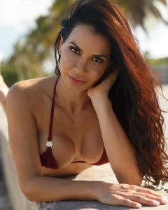 Retrato de cerca en traje de baño color vino, con maquillaje natural y cabello largo oscuro ondulado, en ambiente exterior soleado