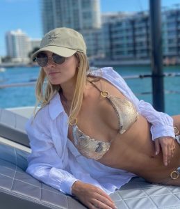 Kika Silva posa con bikini dorado brillante y cover up blanco en un muelle con rascacielos al fondo