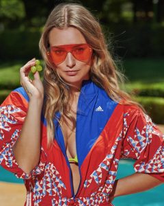 Kika Silva usa lentes de sol rojos y chaqueta deportiva Adidas, posando con uvas verdes