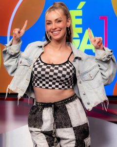 Natalia Rivera sonríe con los brazos extendidos, luce chaqueta denim desgarrada y crop top a cuadros que resaltan su abdomen tonificado