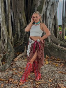 Natalia Rivera posa con confianza en un vestido marrón con abertura lateral, collares y pulseras coloridos, en un entorno natural