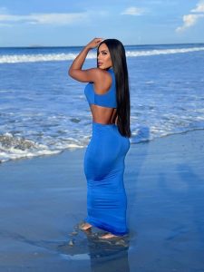Yarishna Ayala posa de perfil con vestido azul ajustado que acentúa su silueta tonificada en la playa