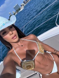 Yarishna Ayala posando en un barco con vista al mar, llevando un bikini blanco con detalles dorados que resalta su figura atlética