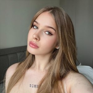 Comatozze modelo rusa creadora contenido, top gris, tatuaje pecho, mirada lateral pensativa